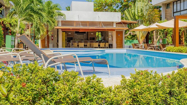 A pool area with lounge chairs, a bar, and a covered seating area.