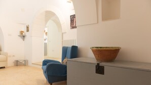 Una habitación con un sillón azul, un armario gris y un recipiente de terracota grande en la parte superior.