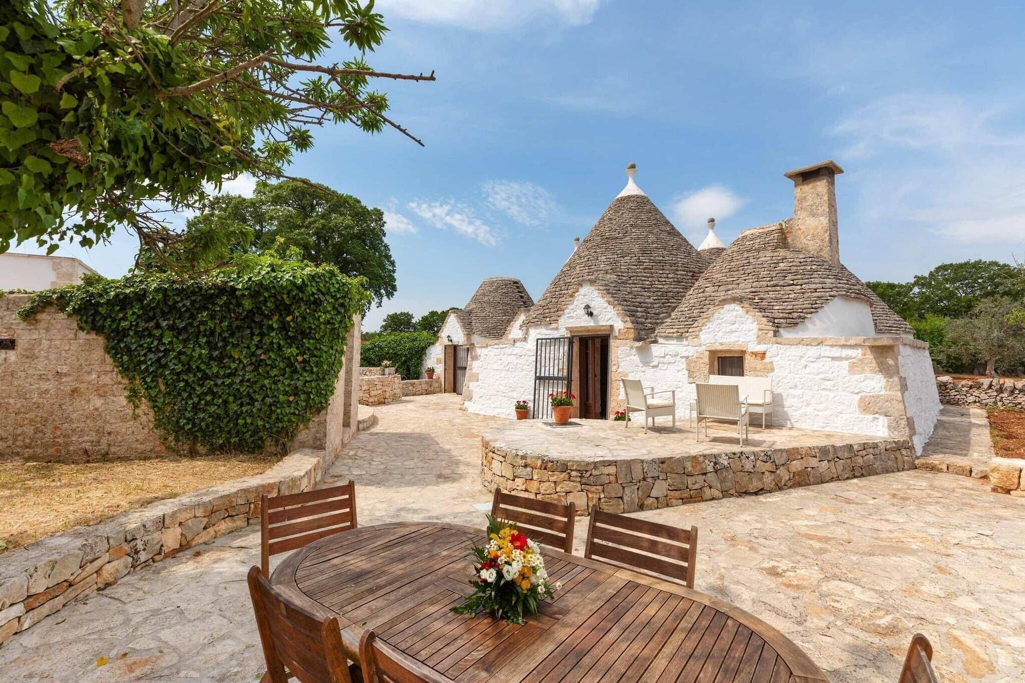 Une maison traditionnelle en pierre dotée d’une terrasse et d’un espace extérieur aménagé pour s’asseoir.