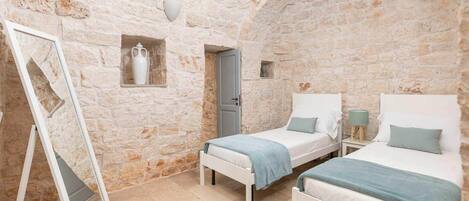 A bedroom with two beds, a mirror, and a stone wall.