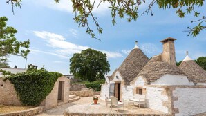 A traditional stone building with a conical roof, a small porch with a bench, and a stone pathway leading to it.