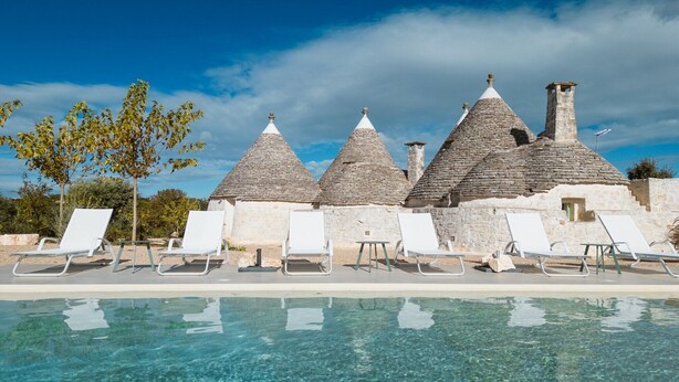A poolside area with stone buildings and white lounge chairs.