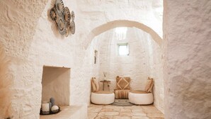 A cozy, rustic interior with a stone floor, a small seating area with cushions and a round table, and a decorative wall piece.