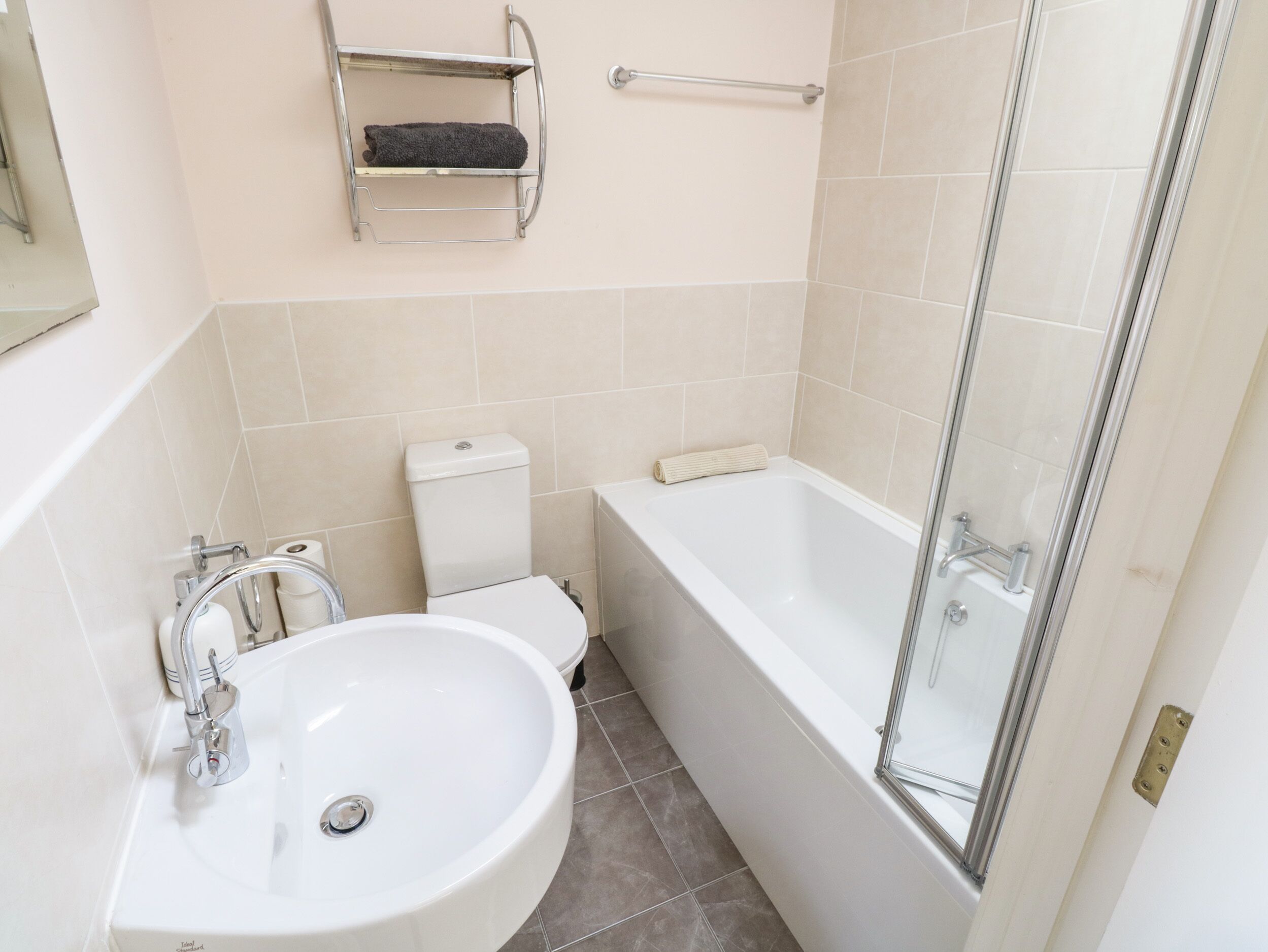 A bathroom with a white sink, toilet, and bathtub. There is a towel rack above the toilet and a glass shower door.