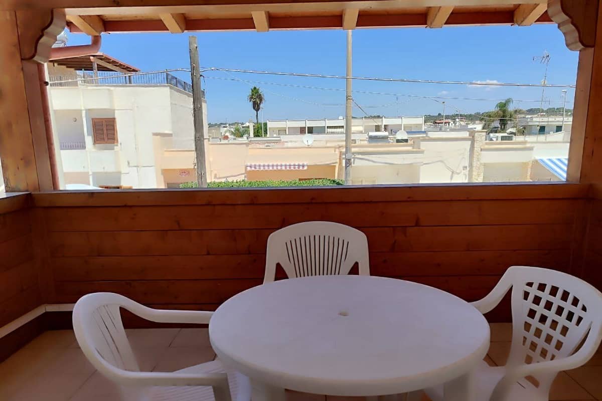 A covered patio with a round table and four white plastic chairs.