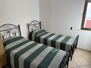 Two single beds with metal frames and green striped bedding in a room with white walls and a tiled floor. - Appartamenti al mare Torre Pali (Salve)