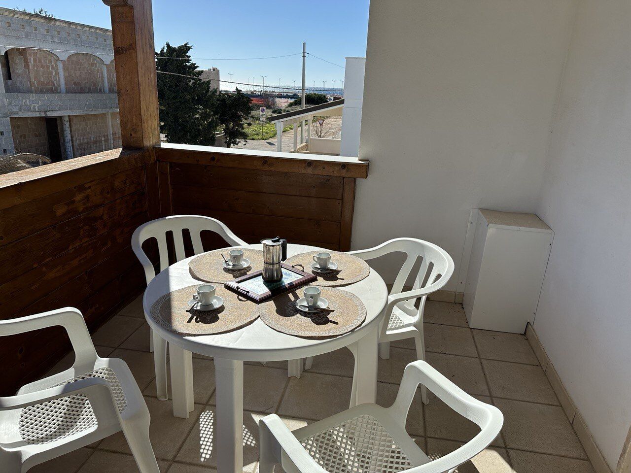 A small outdoor patio with a round table and four chairs, a coffee pot, and a book.