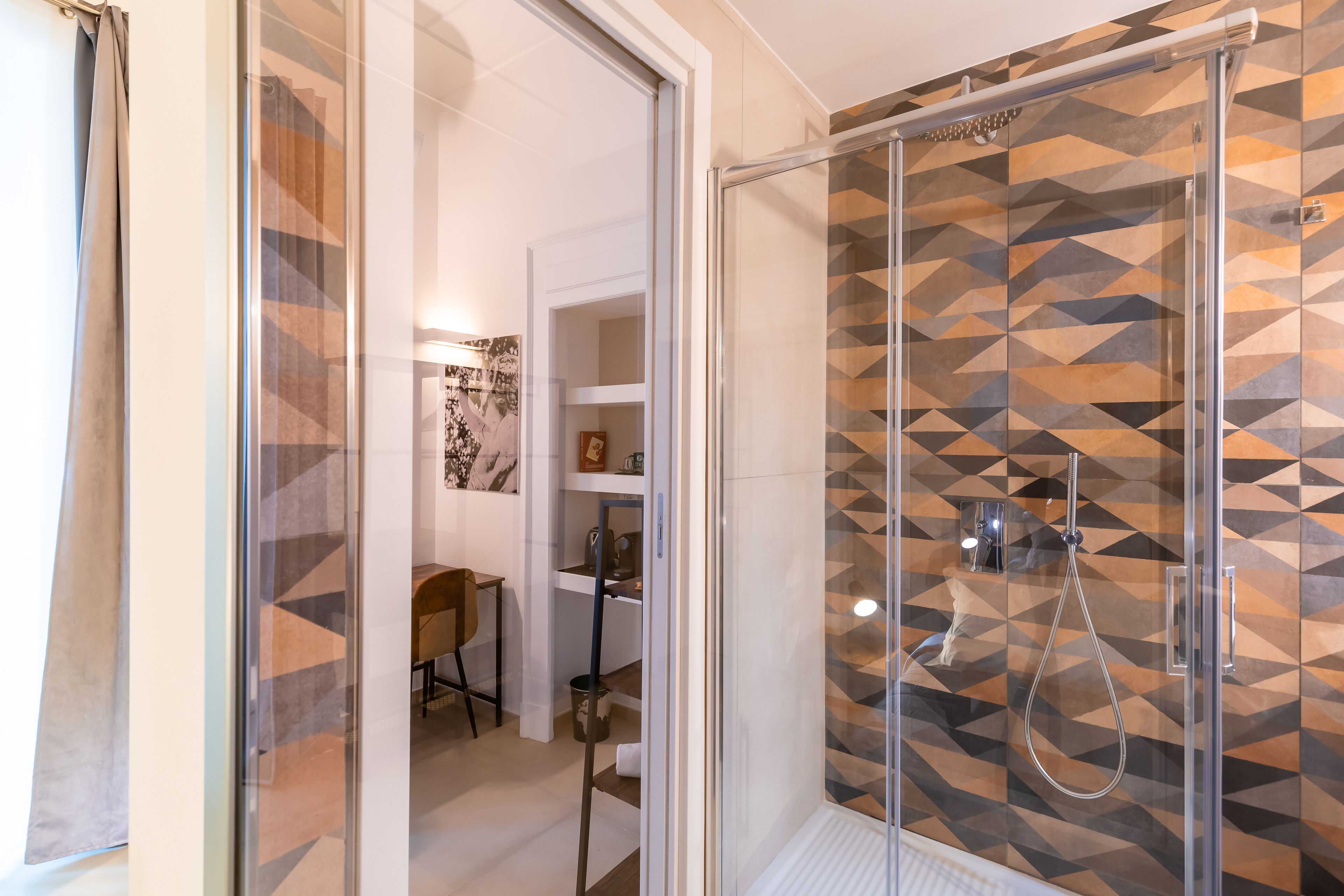 A modern bathroom with a shower area featuring geometric patterned tiles, a glass door, and a visible towel rack.