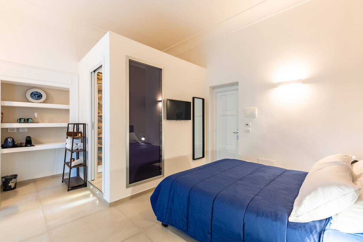 A bedroom with a bed, a wardrobe, a shelf with towels, and a television.
