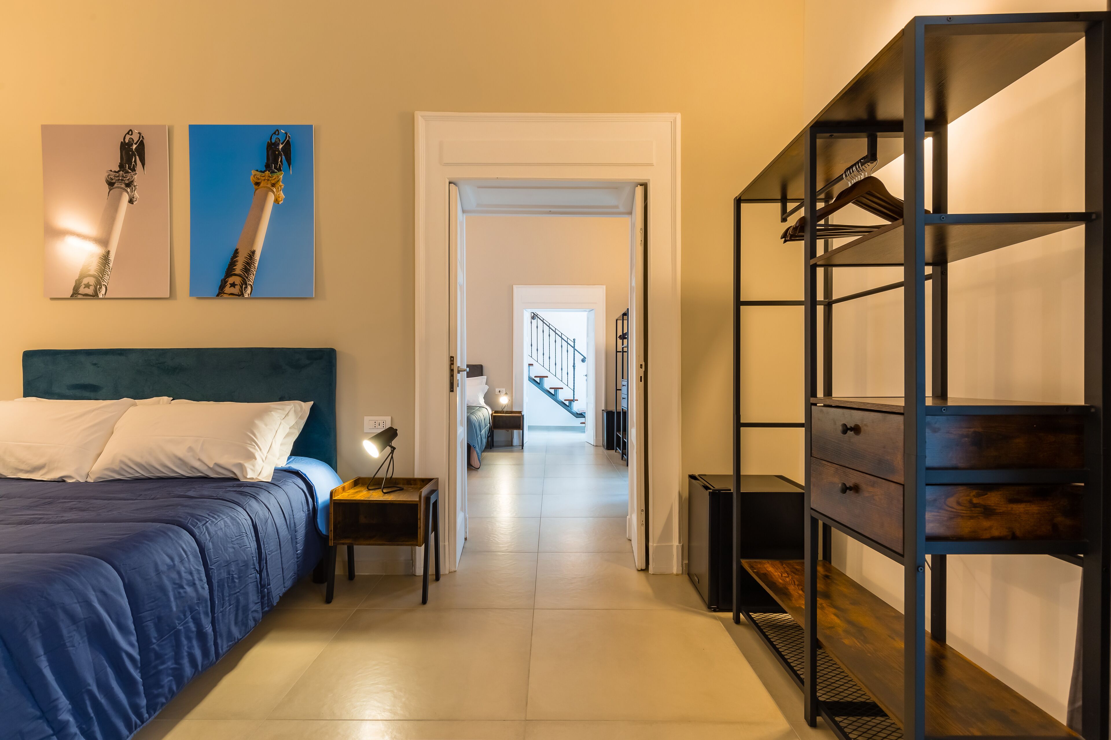 A bedroom with a bed, a nightstand, a wardrobe, and two paintings on the wall.