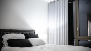 A bedroom with a large bed, a dark headboard, and a sliding glass door leading to a balcony. - Immaculate 2-bed Apartment in Canary Wharf (London)
