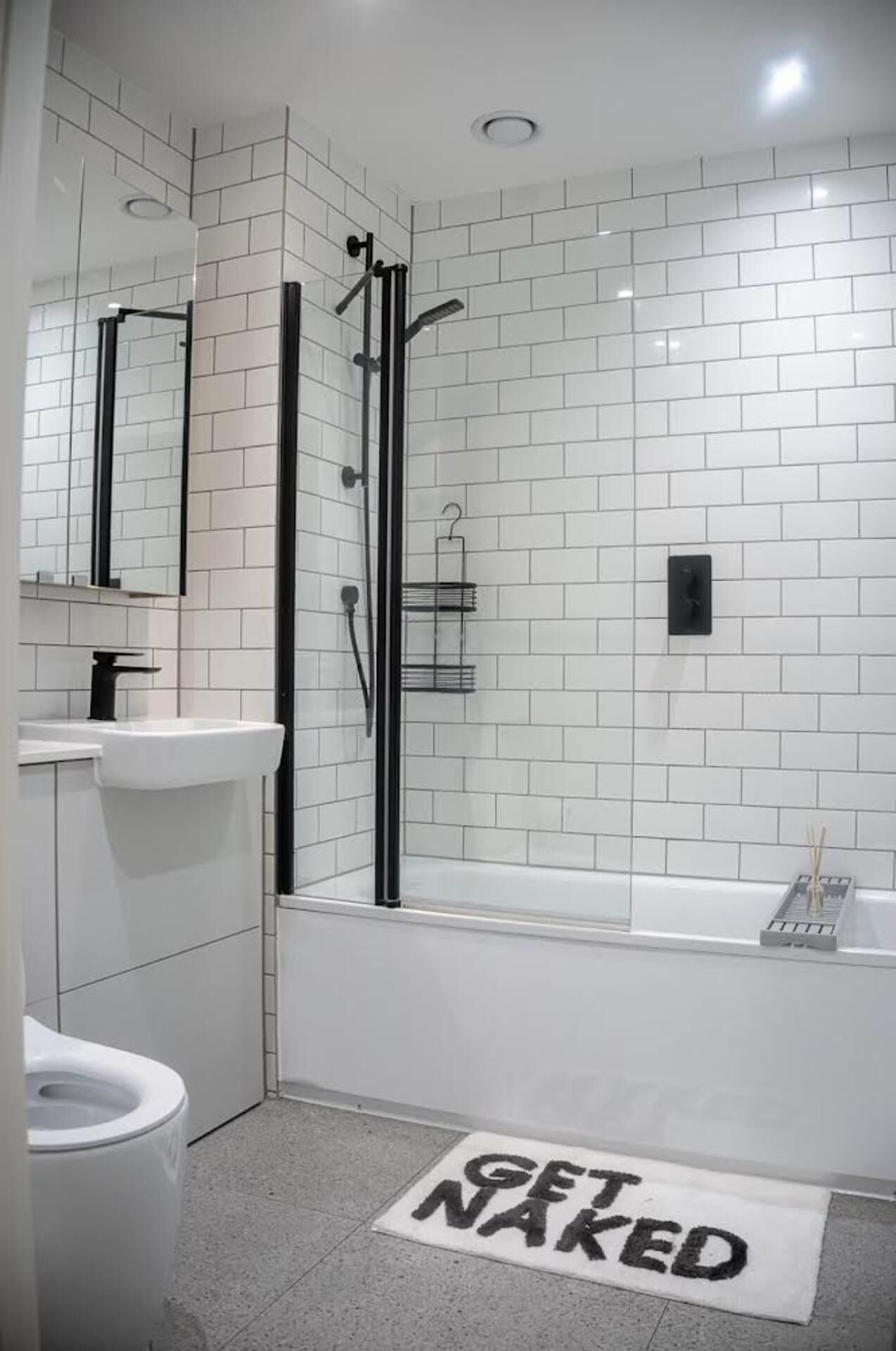 Een moderne badkamer met witte tegels, een glazen douchecabine, een wit wastafelmeubel en een toilet.