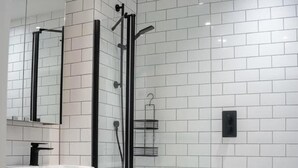 A modern bathroom with white tiles, a glass shower enclosure, a white sink, and a toilet. - Immaculate 2-bed Apartment in Canary Wharf (London)