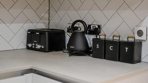 A kitchen with white cabinets, a black toaster, a kettle, and black trash bins labeled S, C, T. - Immaculate 2-bed Apartment in Canary Wharf (London)