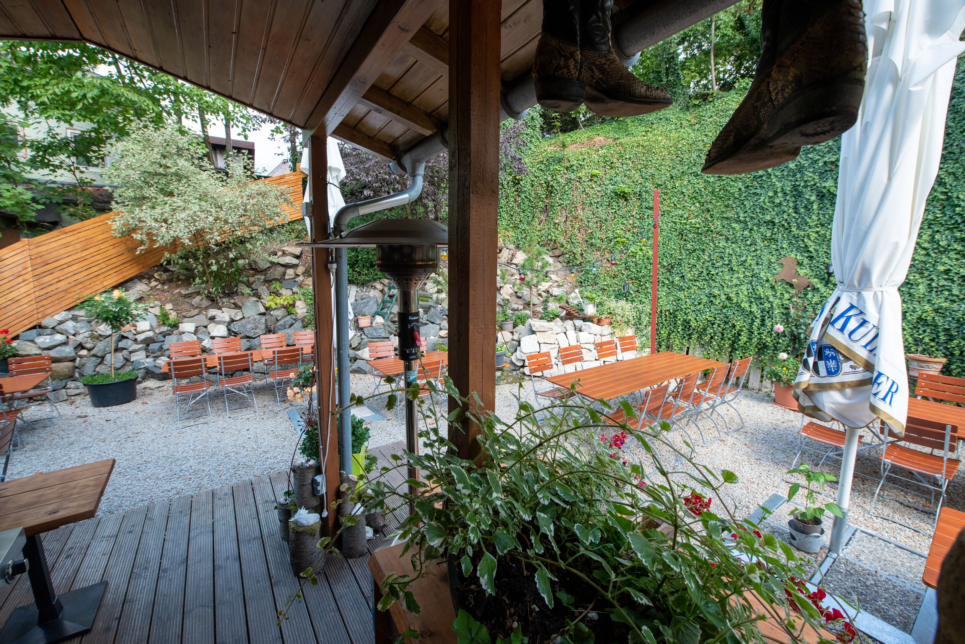 Eine Terrasse im Freien mit Holztischen und -stühlen, einer Steinmauer und verschiedenen Pflanzen.