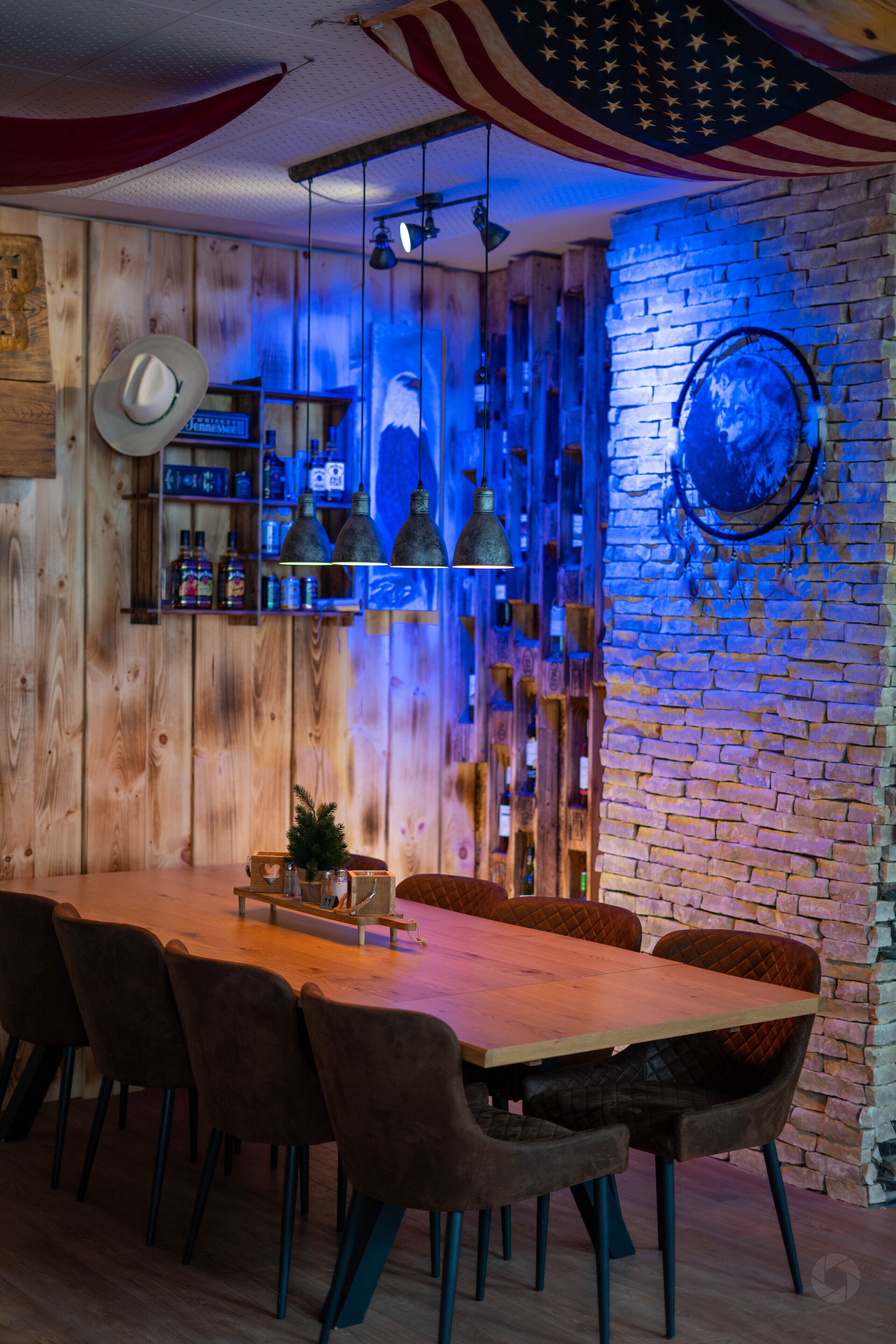 Un intérieur en bois avec un mur en briques, une table en bois entourée de chaises et des lampes suspendues.