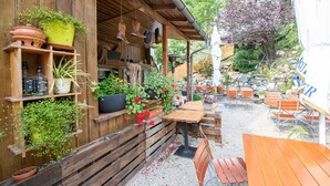 An outdoor seating area with wooden tables and chairs, surrounded by potted plants and a rustic wooden structure.