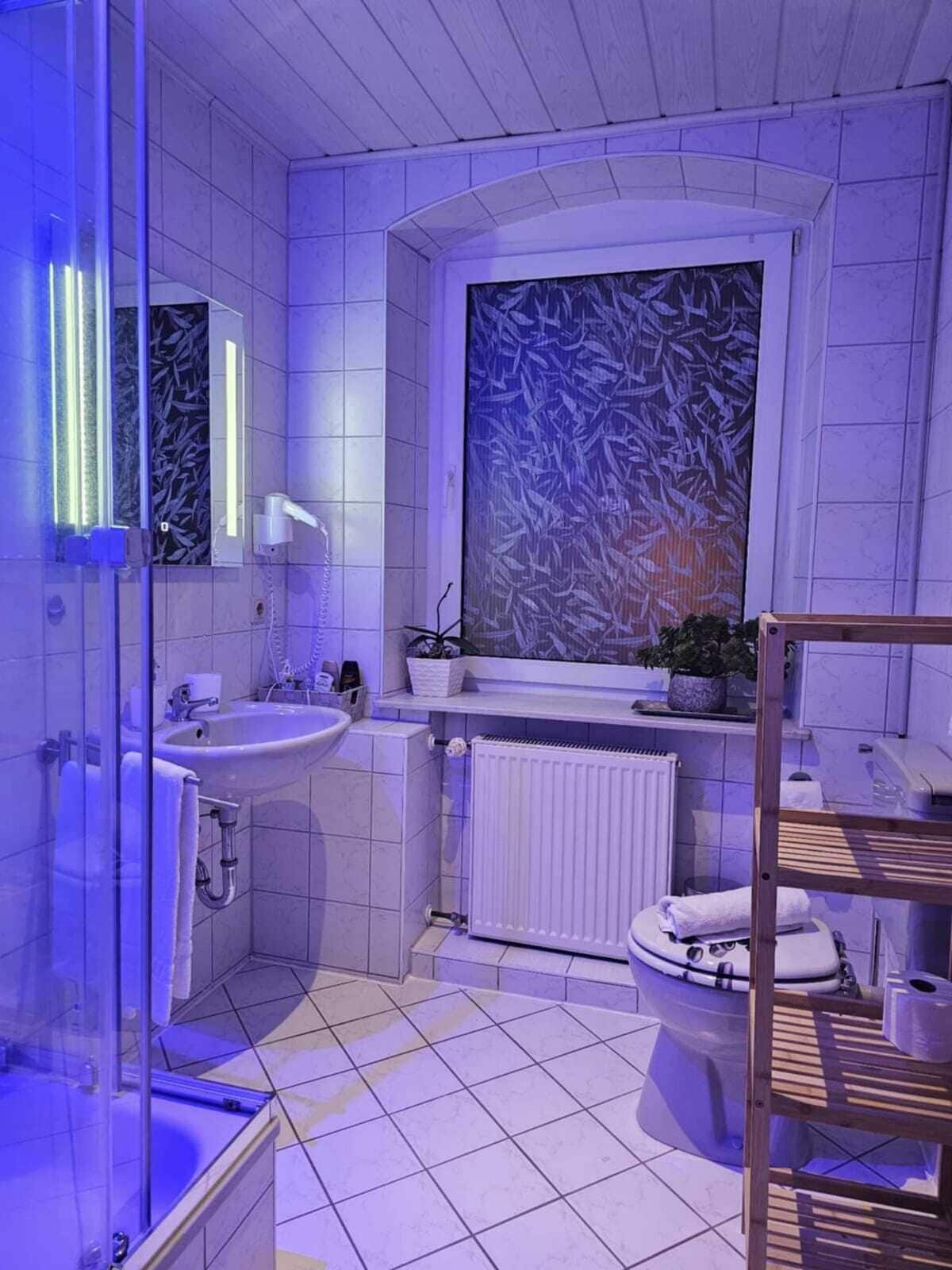 Un baño moderno con cabina de ducha de vidrio, un lavamanos, un inodoro y un ventanal grande con diseño de vidrio esmerilado.