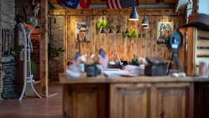 A rustic interior with wooden walls, a central wooden counter, hanging lights, and various decorations including a flag and a painting.