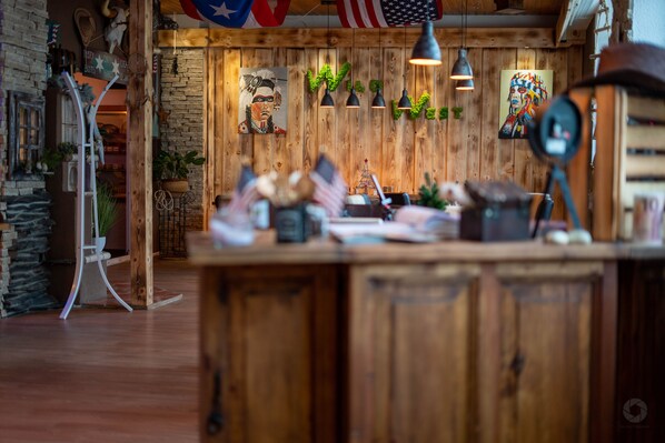 A rustic interior with wooden walls, a central wooden counter, hanging lights, and various decorations including a flag and a painting.