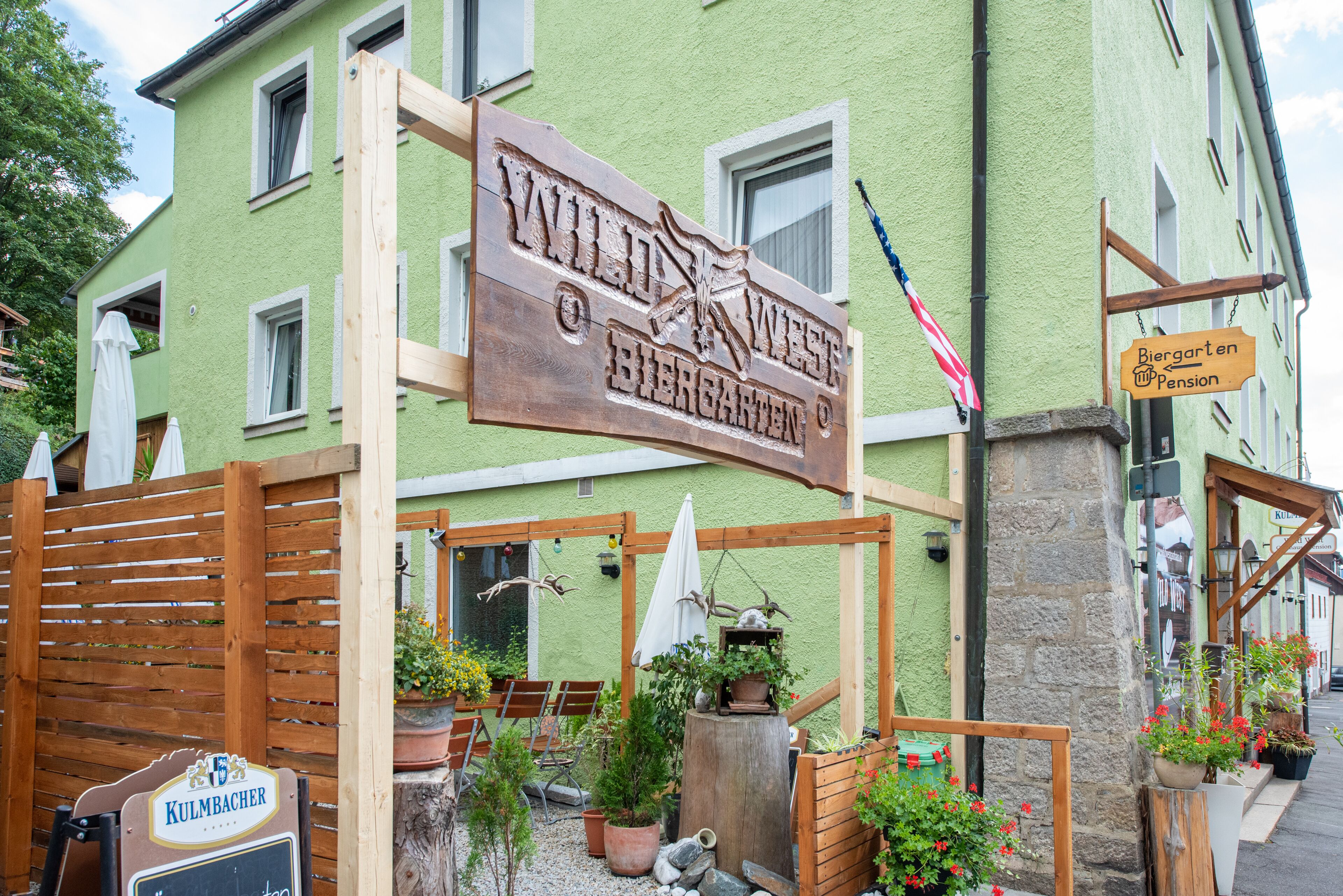A green building with a sign that reads "Wild West Biergarten Pension".