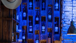 A bar area with wooden shelves filled with bottles, a hat on the left, and a stone wall on the right.