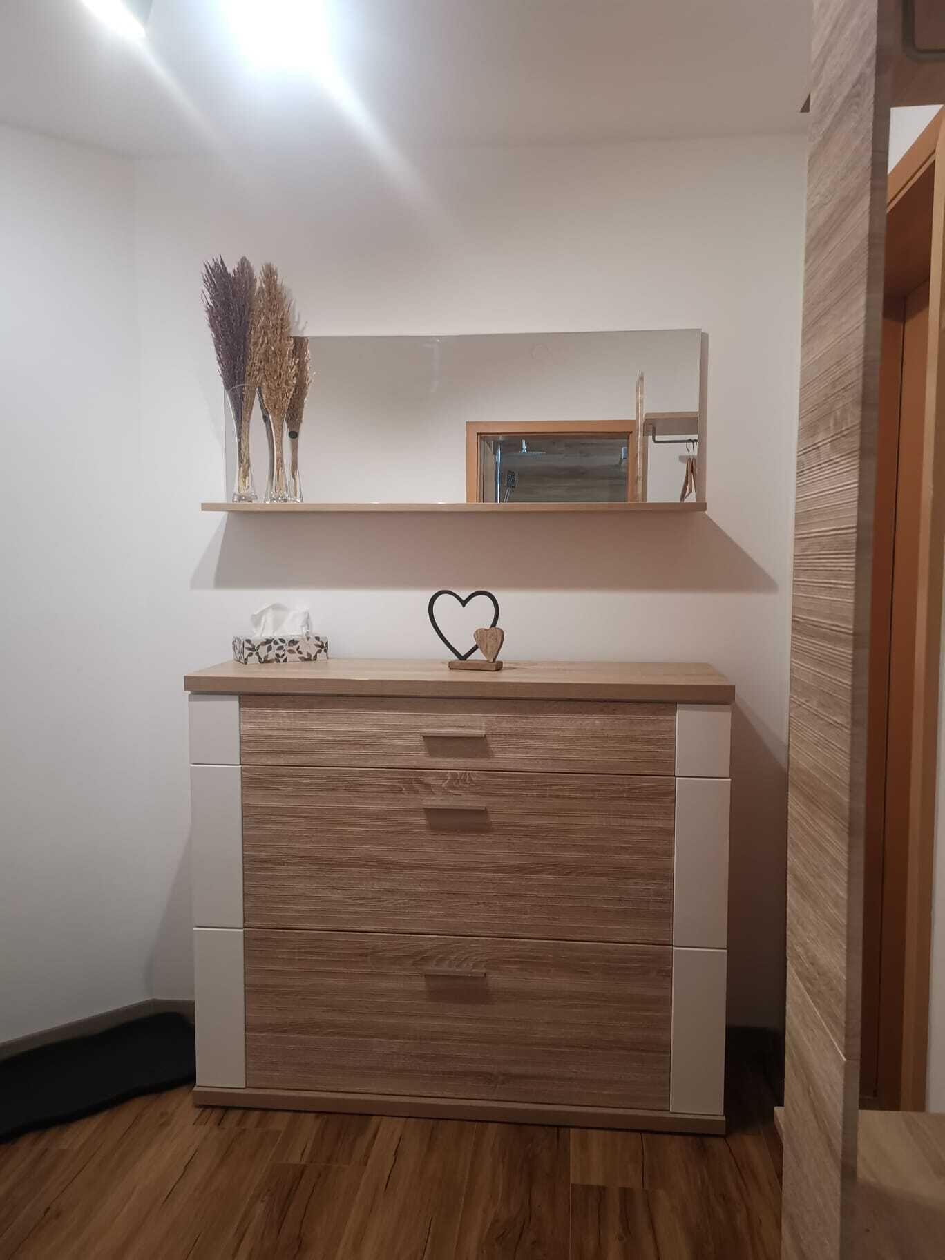 A modern bathroom with a wooden vanity, a mirror, and a small shelf with decorative items.