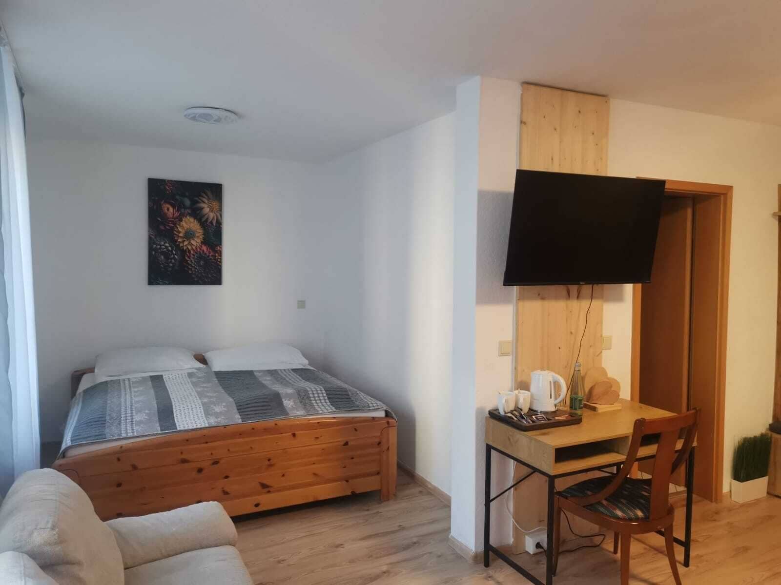 A bedroom with a wooden bed, a desk with a chair, a TV, and a painting on the wall.