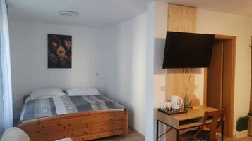 A bedroom with a wooden bed, a desk with a chair, a TV, and a painting on the wall.