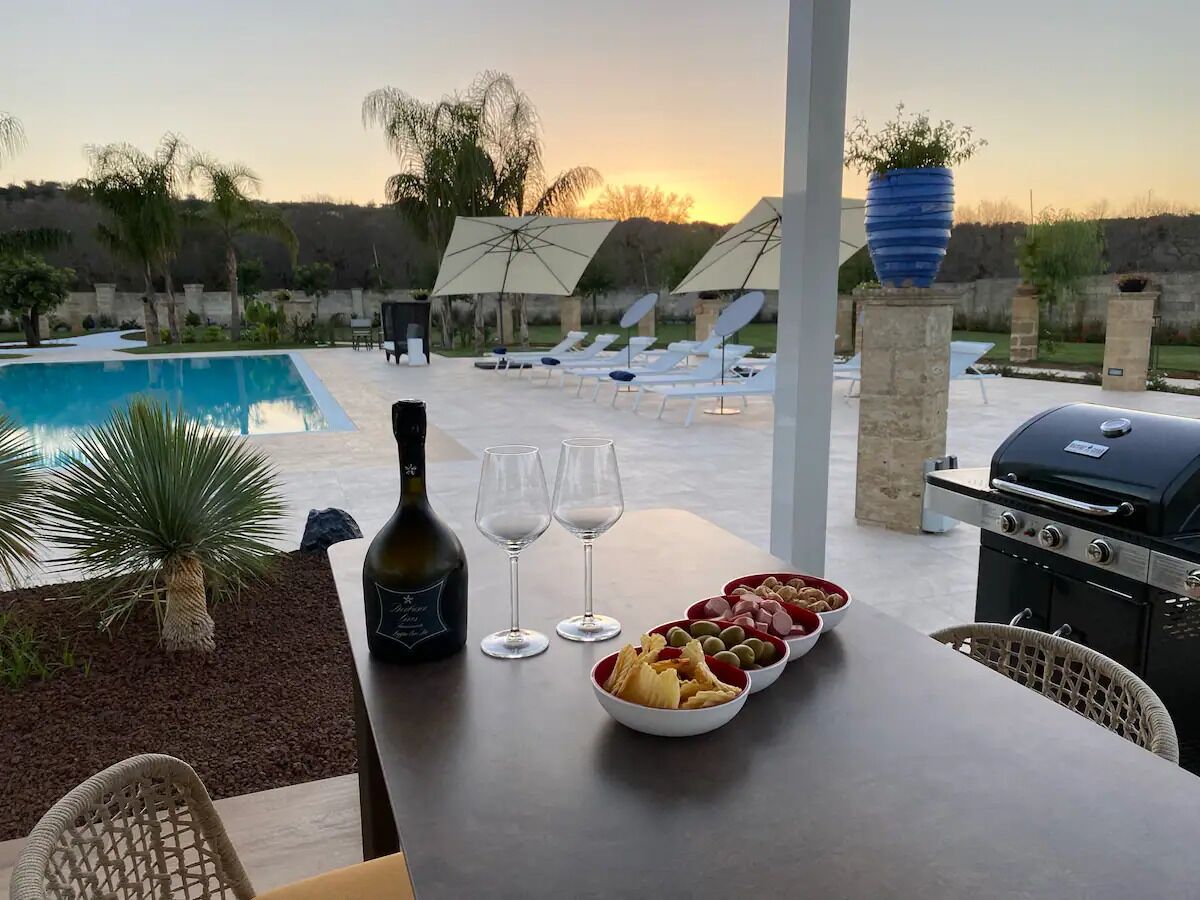 Un espace repas aménagé au bord de la piscine, avec une table dressée pour un repas, un barbecue et des chaises longues.