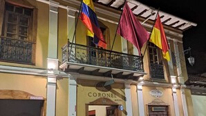 Um hotel com varanda, um letreiro com a inscrição 'CORONEL HOTEL' e bandeiras penduradas na varanda.