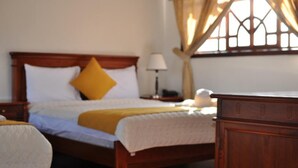 Quarto de hotel com cama de madeira, mesa de cabeceira, luminária e janela com cortinas.