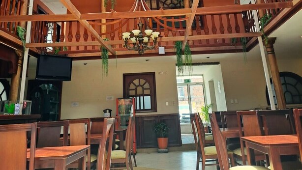 Um átrio com vários níveis, balaústres de madeira, plantas pendentes e um candelabro.