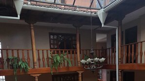 Um átrio em vários níveis com guarda-corpos de madeira, plantas pendentes e um candelabro.
