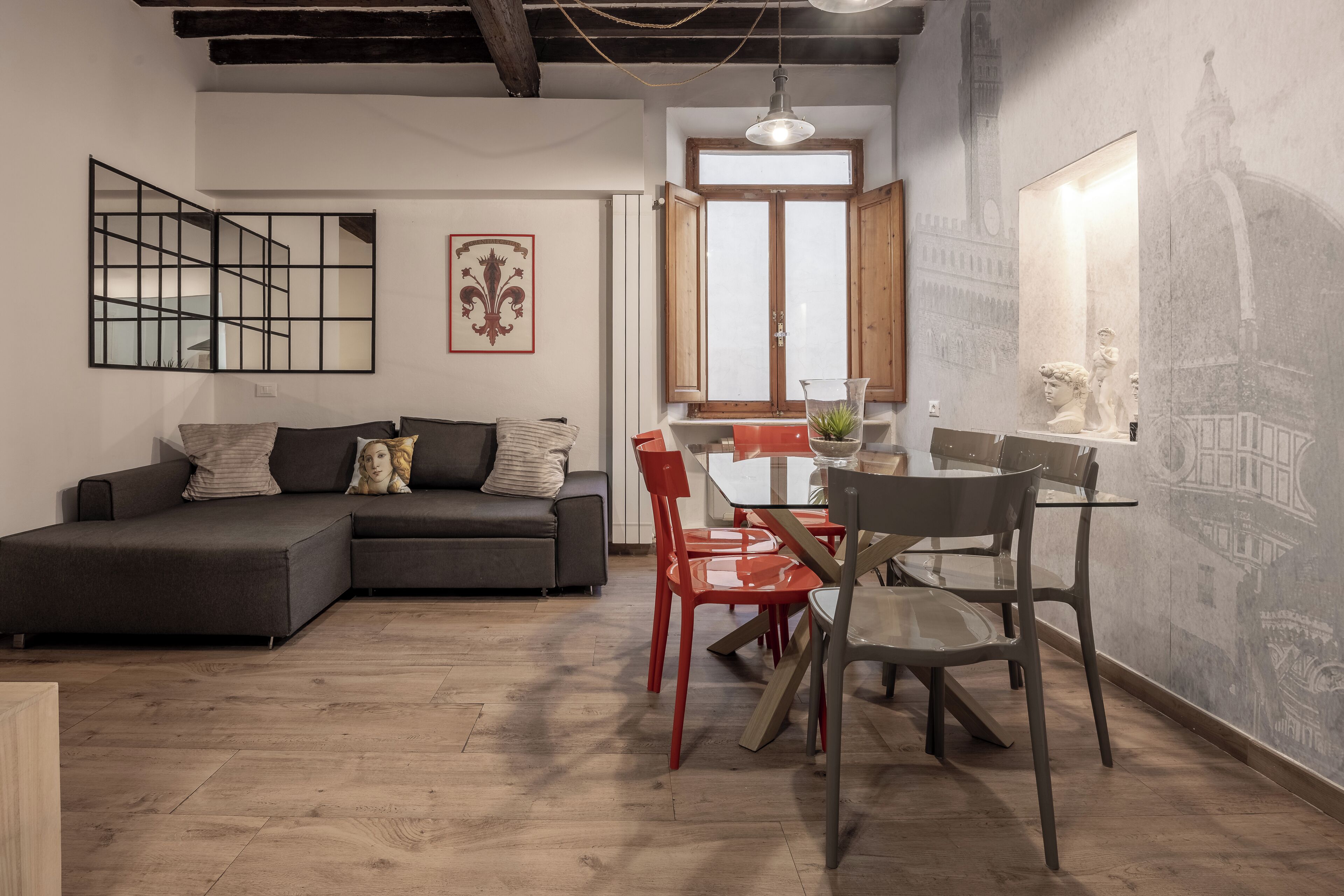 Ein modernes Wohnzimmer mit einem Ecksofa, einem Esstisch mit roten Stühlen und einem großen Fenster mit Blick auf einen Kirchturm.