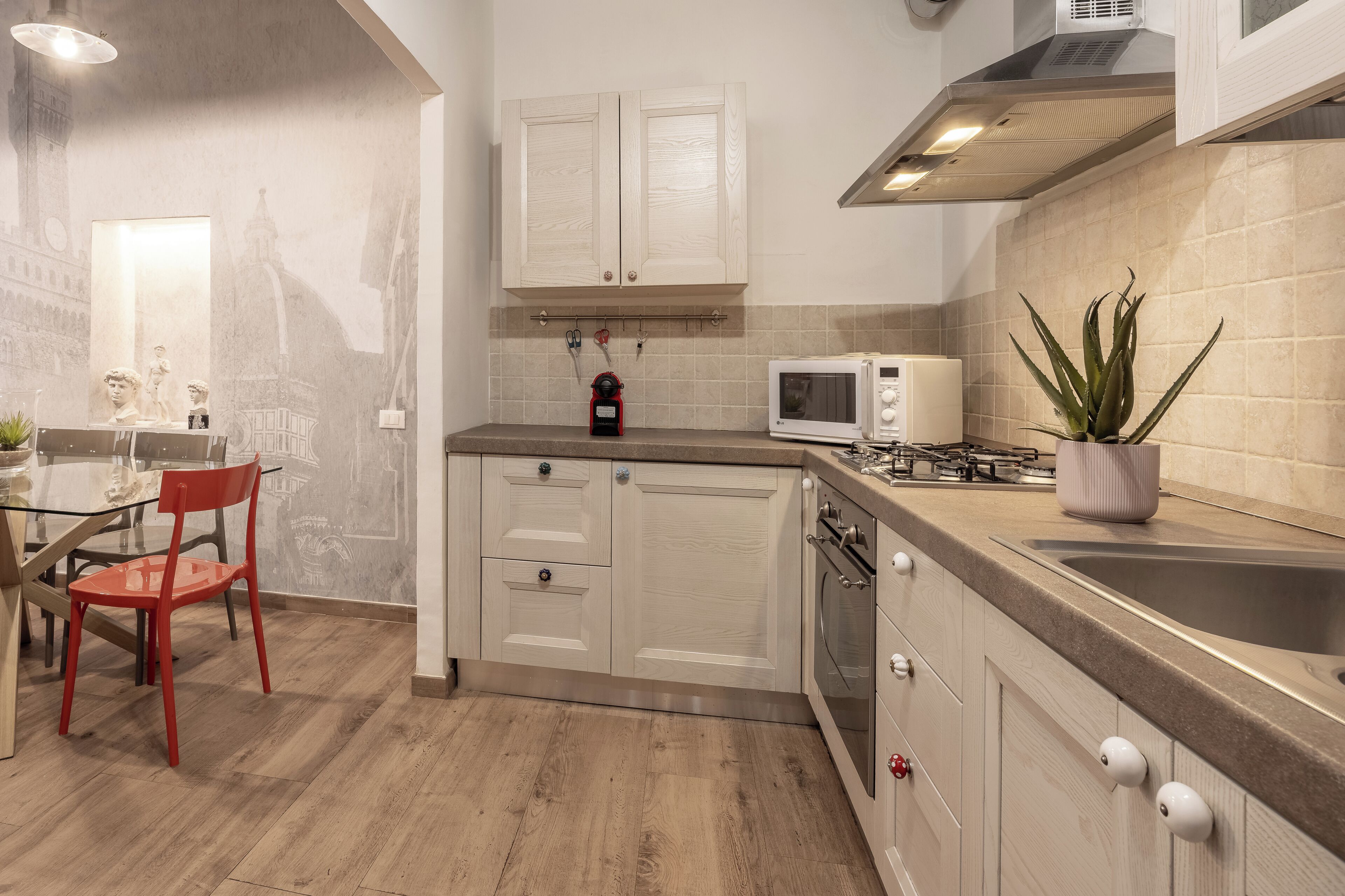 A modern kitchen with white cabinets, a microwave, a sink, and a red chair.