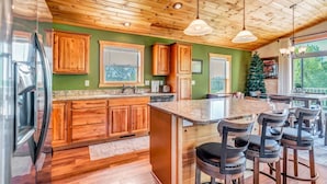 Une cuisine avec des meubles en bois, un grand îlot central doté de tabourets, et une vue sur l’extérieur.