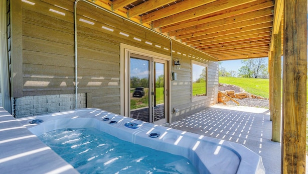 Un espace avec un bain à remous, une terrasse en bois, un patio couvert et une vue sur un champ verdoyant.