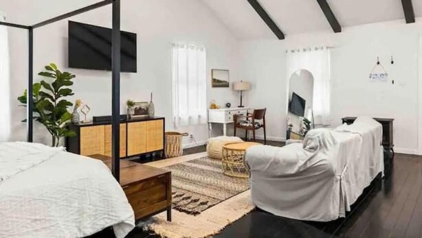 A bedroom with a four-poster bed, a desk, a chair, and a TV mounted on the wall. - Cozy, private and modern Cottage (Hudson)