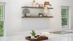 A modern kitchen with a marble countertop, built-in shelves, and a window providing natural light. - Cozy, private and modern Cottage (Hudson)