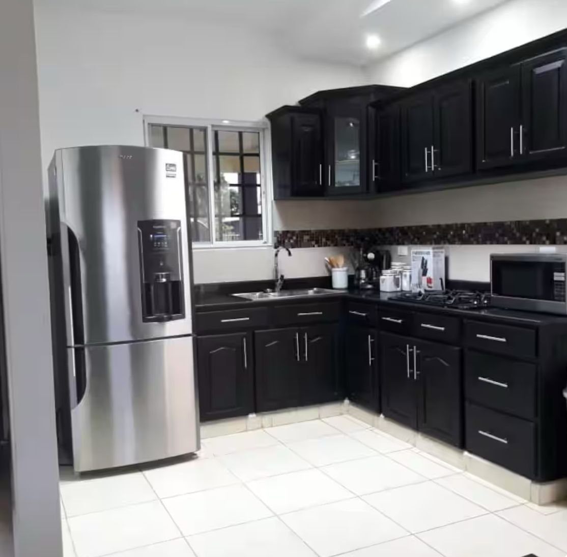 Una cocina moderna con armarios negros, electrodomésticos de acero inoxidable y piso de baldosas.