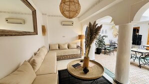 A modern living room with a beige sofa, a round woven coffee table, and a potted plant. - Riad Sarah Sabrina (Marrakech)