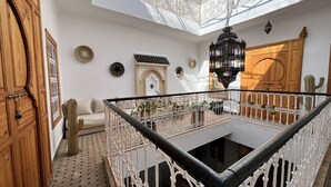 A spacious interior with a high ceiling, a central black-tiled area, white ornate railings, and a wooden door. - Riad Sarah Sabrina (Marrakech)