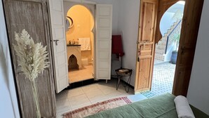 A bedroom with a green bedspread, a white towel, a wooden door, and a view of a tiled outdoor area. - Riad Sarah Sabrina (Marrakech)