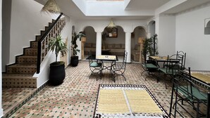 A spacious interior with a high ceiling, a central seating area with a table and chairs, and a staircase with decorative railings. - Riad Sarah Sabrina (Marrakech)
