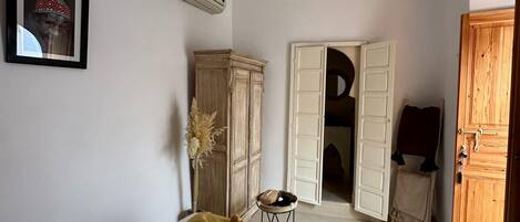 A bedroom with a bed, a wardrobe, an open door leading to another room, and a small table with a basket.