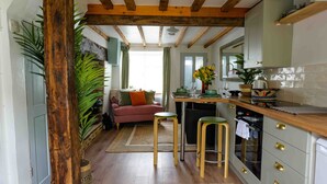 A kitchen with wooden beams, a dining area with stools, a sofa, and a large plant. - Cosy 1 bedroom cottage in The Cotswolds (Chipping Norton)