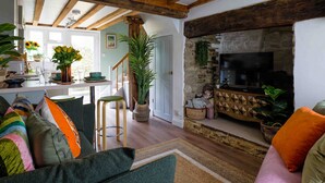 A cozy living room with a fireplace, wooden beams, and a dining area with a view of the kitchen. - Cosy 1 bedroom cottage in The Cotswolds (Chipping Norton)