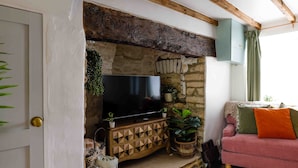 A cozy living room with a stone fireplace, a flat-screen TV, and a pink sofa. - Cosy 1 bedroom cottage in The Cotswolds (Chipping Norton)