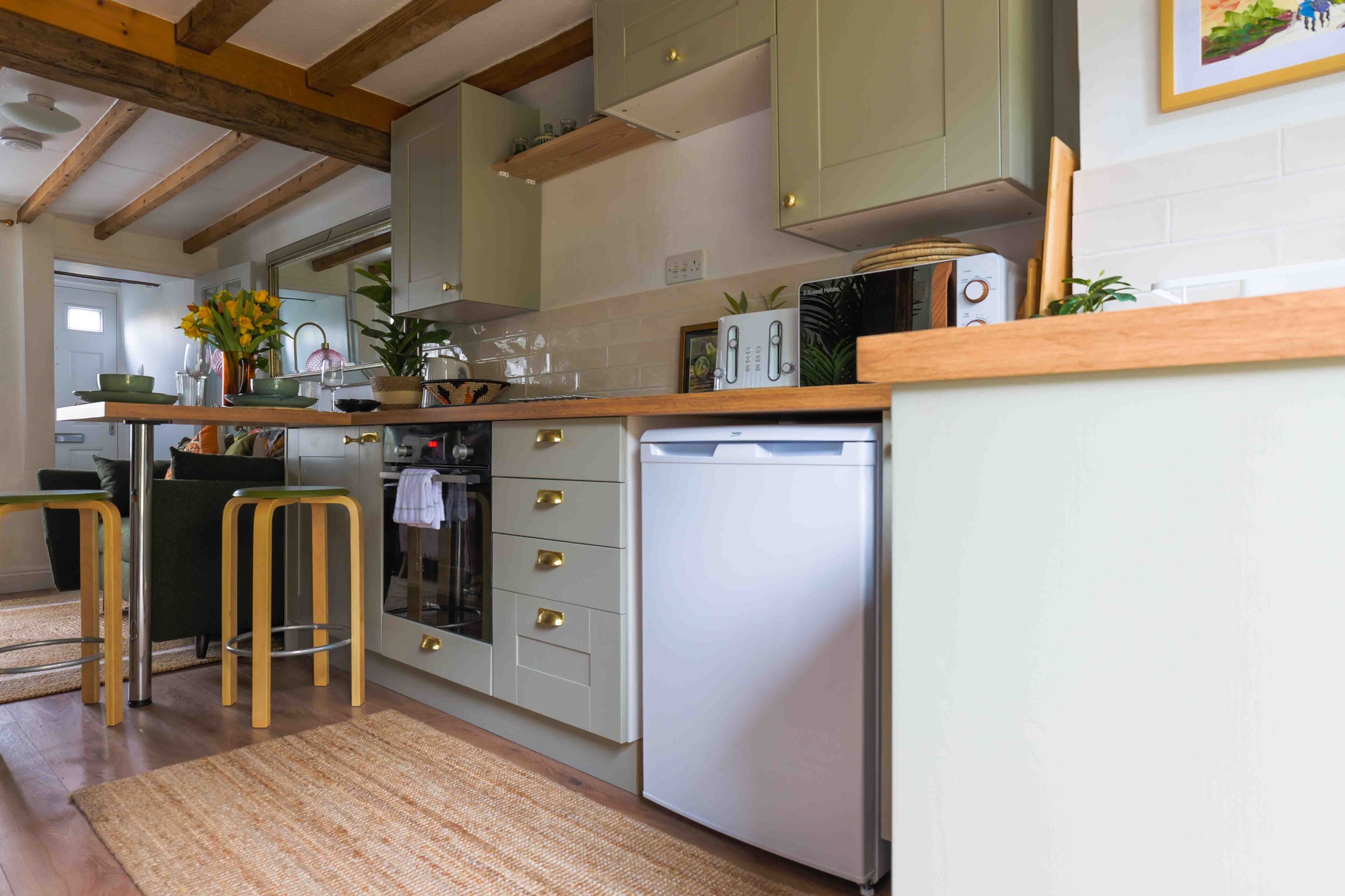 A kitchen with wooden beams, a refrigerator, a stove, and bar stools.